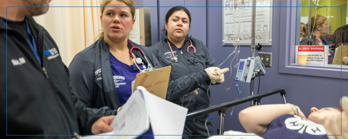 Healthcare students practicing patient care in a clinical training lab with a simulation mannequin