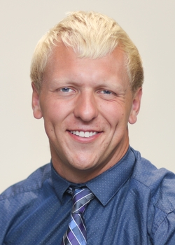 Photo of Nick Schlitz wearing a blue shirt and tie, smiling